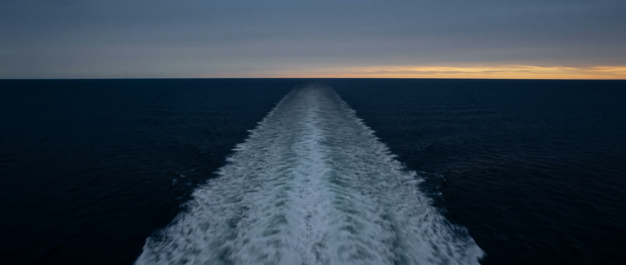 The wake of a vessel trailing away across open water at dusk.
