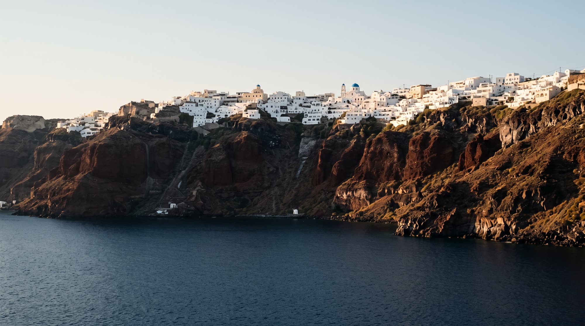 The Santorini caldera at golden hour, seen from the water.